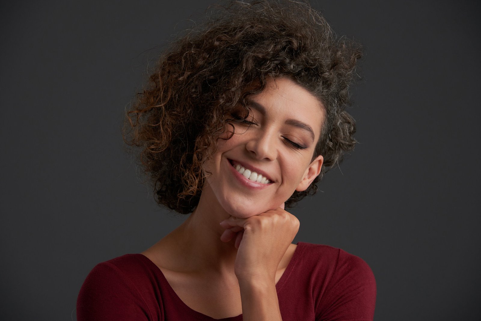 Smiling happy woman with her eyes closed, isolated on grey